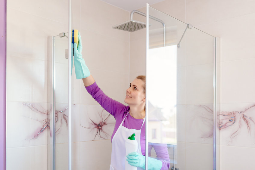 Young beautiful woman in white apron cleaning shower cabin