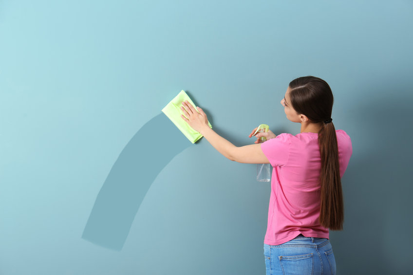 Young woman wiping color wall with rag.