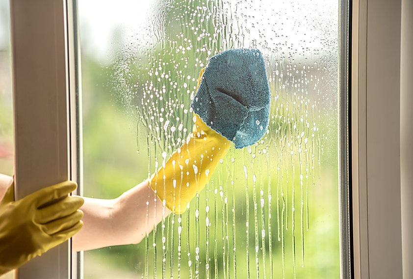 A female hand in a yellow glove washes a dirty window in the summer