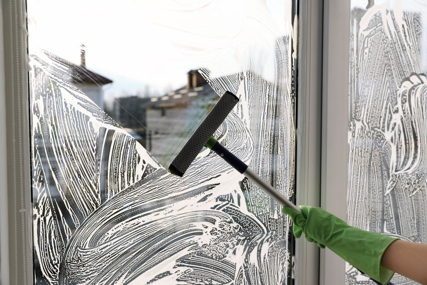 Woman cleaning window with squeegee indoors, closeup