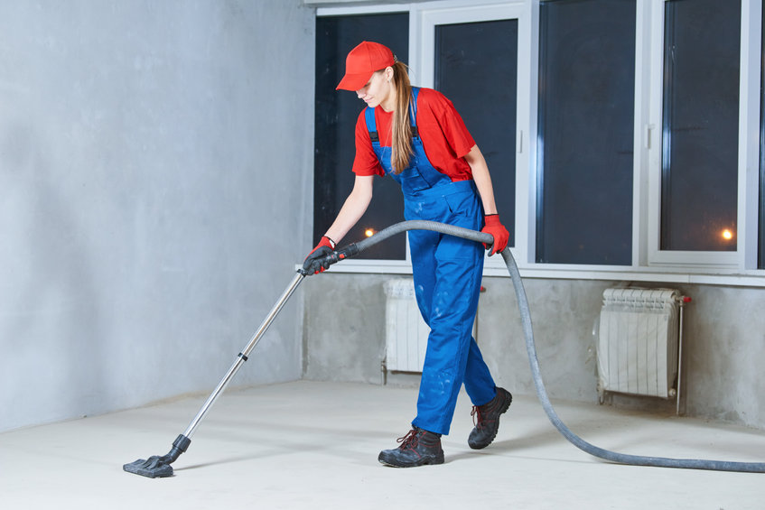 young woman cleaning and removing construction dust with vacuum cleaner after repair