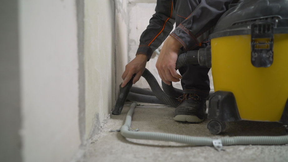Worker washes the floor with a vacuum cleaner from industrial concrete dust and cement mud during home renovation. 