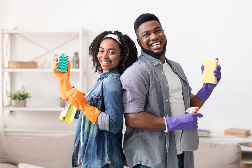 Cheerful couple posing with cleaning supplies while doing housework together
